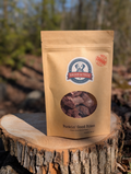 Kraft paper bag of 'Dried & True' dog treats on a wooden stump with a natural background