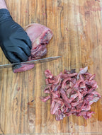 Person cutting raw meat on a wooden cutting board with a knife.