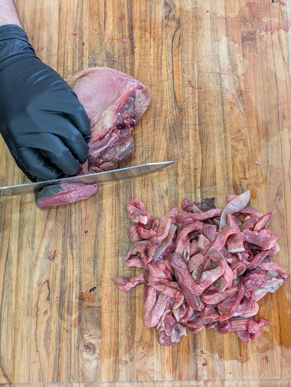 Person cutting raw meat on a wooden cutting board with a knife.