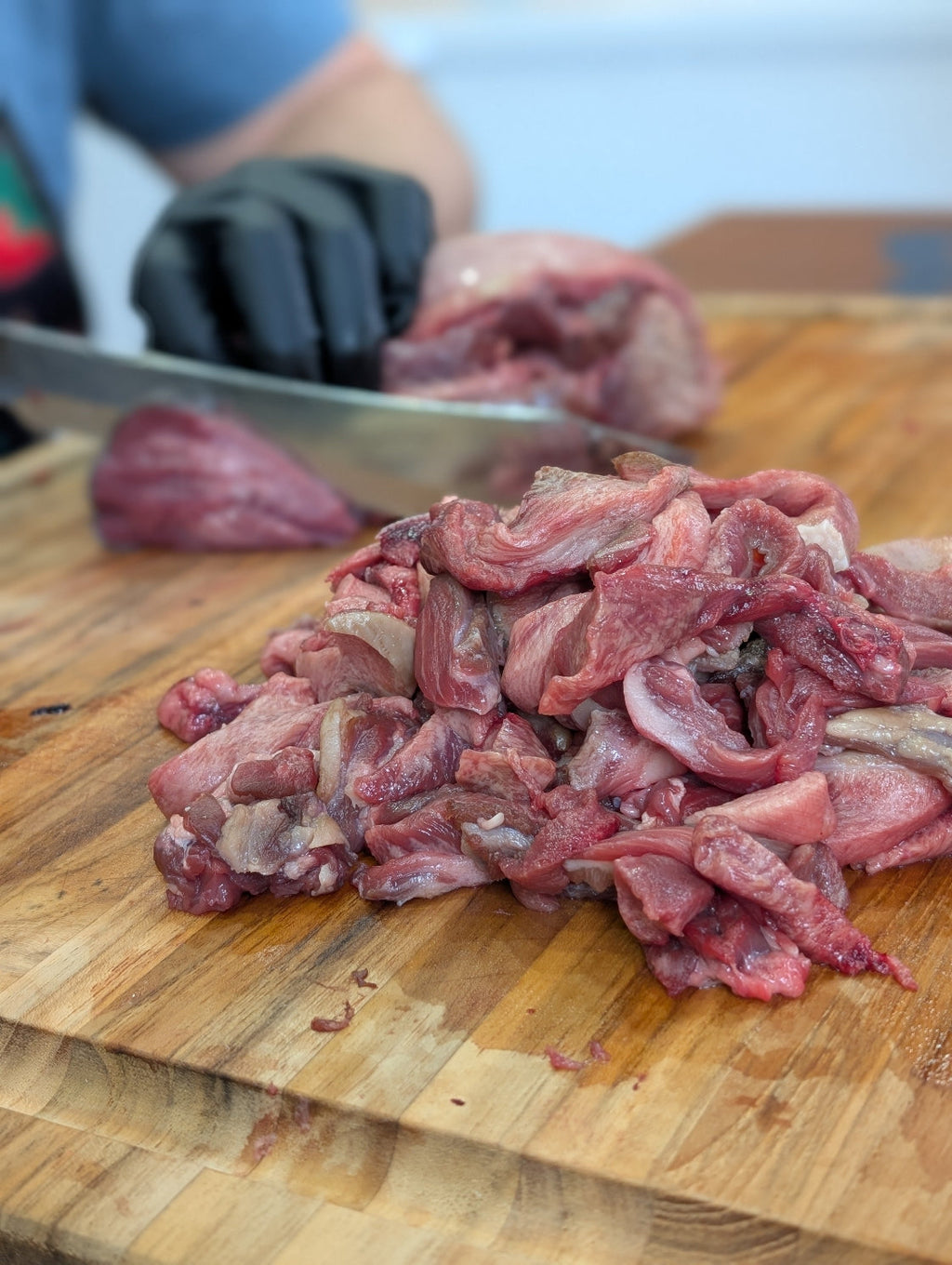 Raw meat on a wooden cutting board with a person in the background.