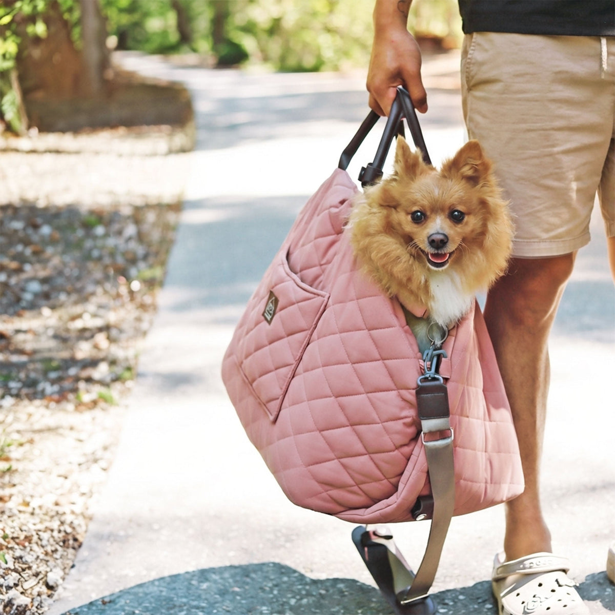 Person walking on the street with a pink quilted pet carrier with a dog inside