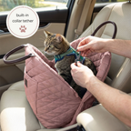 Cat in a pink car seat with a person adjusting a collar tether, inside a vehicle.