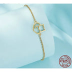 Gold bracelet with a heart and chain design on a light blue background, featuring a 'Real Sterling 925' stamp.