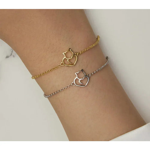 Two cat-shaped bracelet charms on a wrist against a neutral background