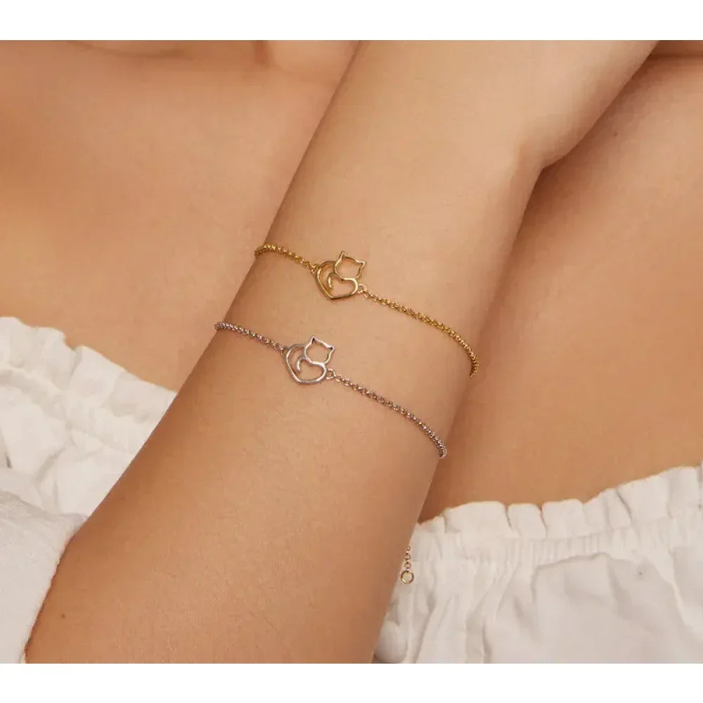 Two gold and silver cat-shaped bracelets on a person's wrist against a neutral background.