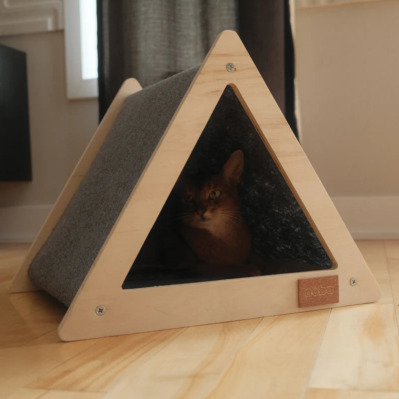 Triangular pet bed with a cat peeking out on a wooden floor
