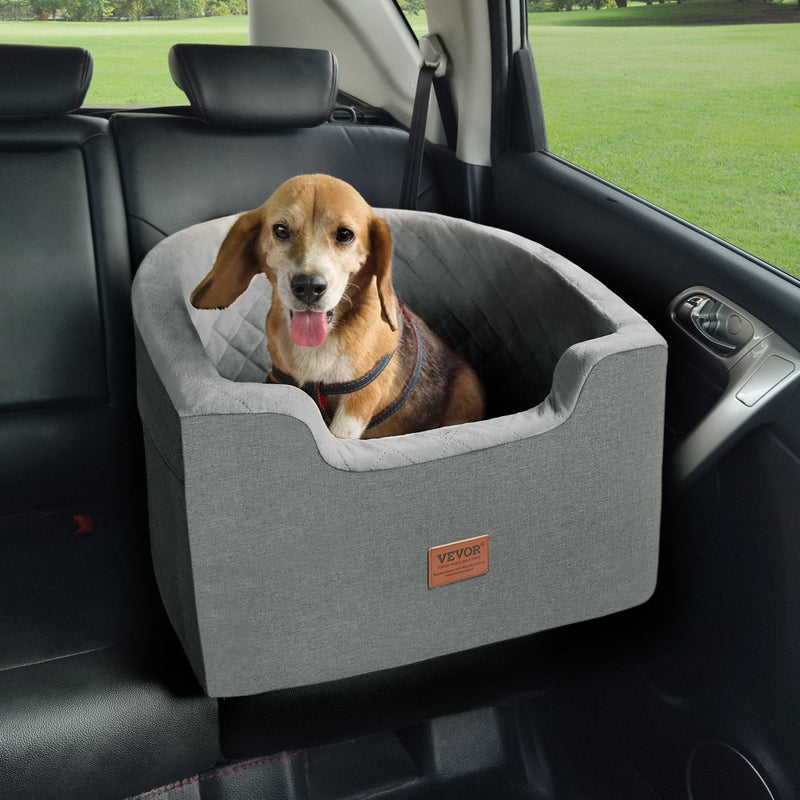 Dog sitting in a gray pet seat in a car with a green field outside.