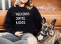 Person wearing a black sweatshirt with 'WEEKENDS. COFFEE. & DOGS.' text, sitting on a couch with a dog.
