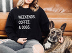 Person wearing a black sweatshirt with 'WEEKENDS. COFFEE. & DOGS.' text, sitting on a couch with a dog.